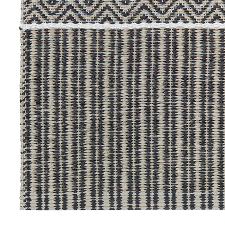 Close-up of the Alfie - Graphite vinyl rug by Horredsmattan showcasing a woven textile pattern with horizontal and vertical black and beige stripes and a geometric design at the top, crafted as an environmentally friendly PVC Swedish product.