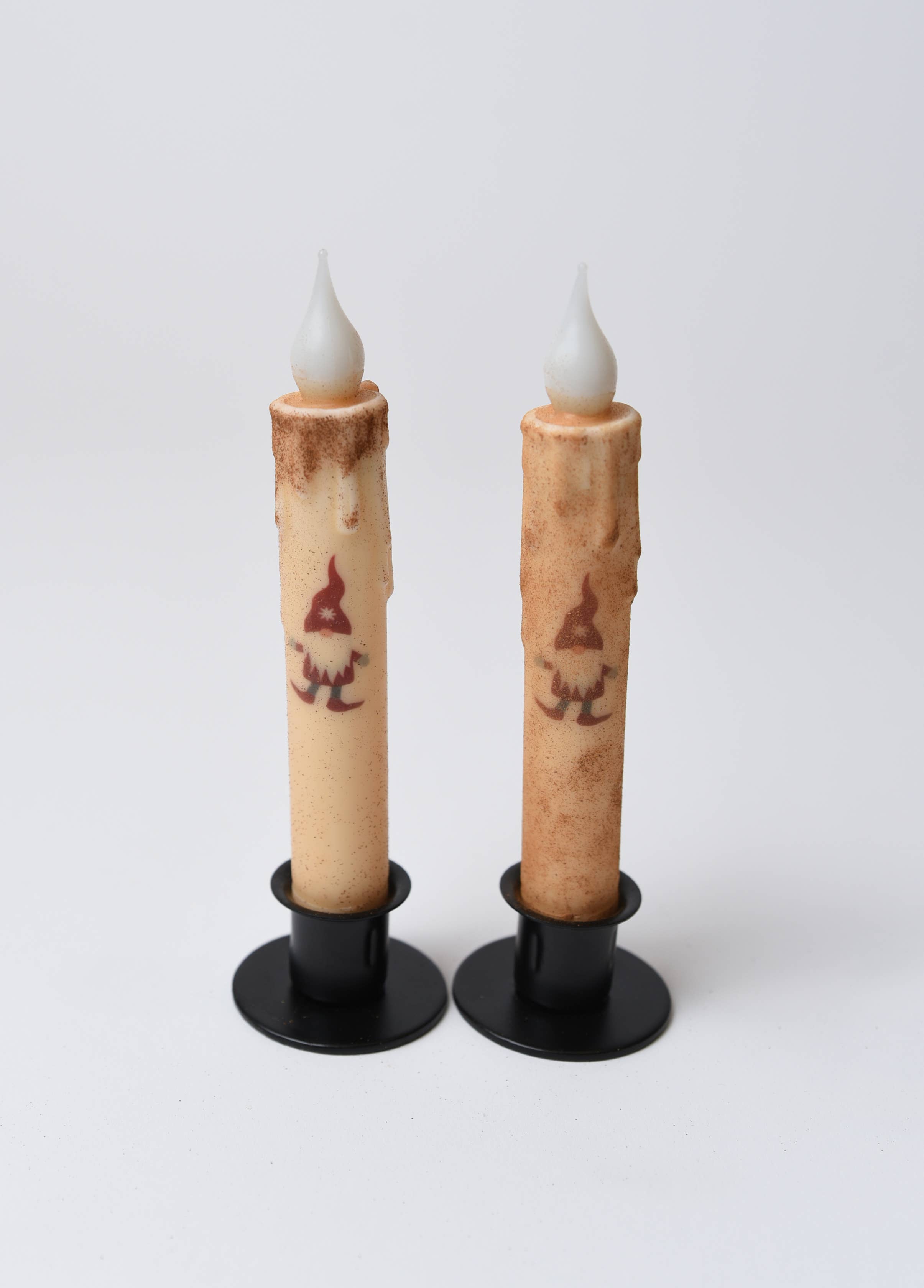 Two Cinnamon Dusted Christmas Gnome LED timer taper candles with Santa faces and artificial wax drips stand in black holders on a white background, adding festive charm to your decor.