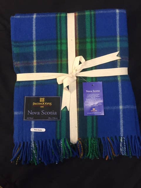 A folded blue, green, and white Nova Scotia Deluxe Highland Tartan Blanket - Merino Wool is tied with a cream ribbon and features two attached product tags.