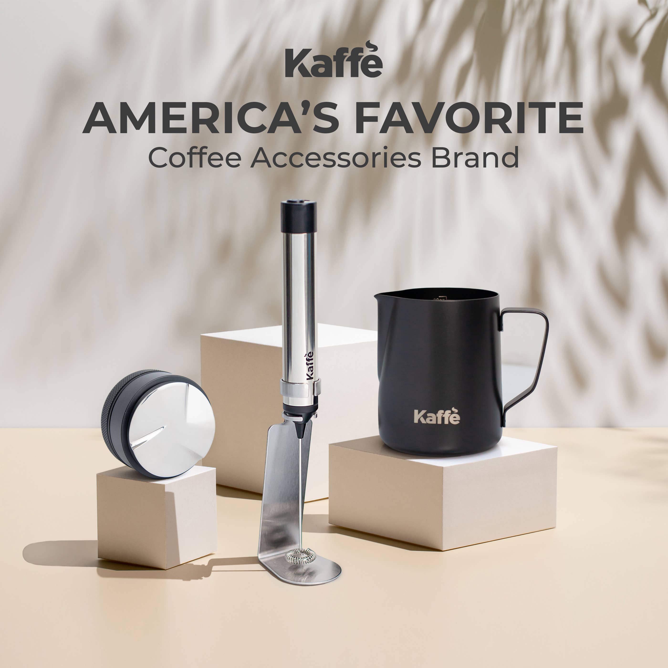 Three Kaffe coffee accessories—a grinder, tamper, and the Kaffe Handheld Milk Frother with Stand (USB Rechargeable, Stainless Steel)—sit on light blocks with “America’s Favorite Coffee Accessories Brand” above them.