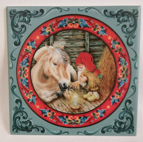 The 6" ceramic tile, "Fjord Horse with Tomte," shows a gnome in red sitting with a horse by candlelight in a stable, framed by rosemaling art—perfect Scandinavian holiday décor. Cork backing included.
