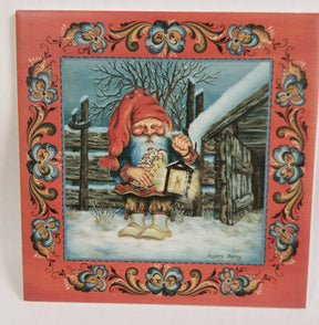 The 6x6 "Tomte with Logs and a Lantern in the Snow" tile features a gnome in red with a lantern and logs, standing in snow by a fence and cabin, framed by Norwegian rosemaling. Includes cork backing and hanger.