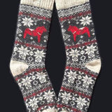 Swedish Passport Co's Socks: Red Dala Horse Black and Natural Wool Socks by Viking Knits feature a black, white, and red snowflake pattern with a Swedish Dala Horse on each sock, made from 70% wool. Displayed against a black background.