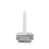 A white candle stands upright in the Stumpastaken Ettan candle holder, made from 100% recycled material and finished in white powdercoat (8.8x8.8x4 cm), against a white background.