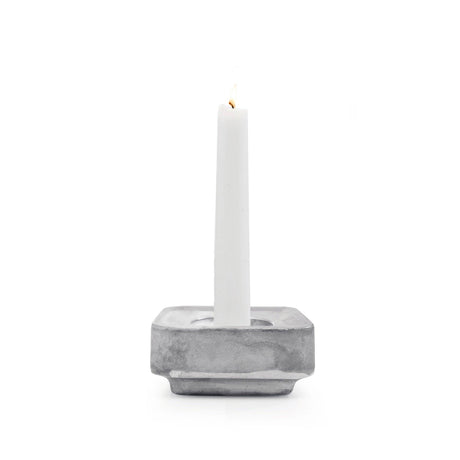 A white candle stands upright in the Stumpastaken Ettan candle holder, made from 100% recycled material and finished in white powdercoat (8.8x8.8x4 cm), against a white background.