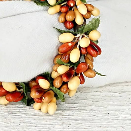 Napkin ring decorated with clusters of cream and reddish-brown pip berries and green leaves.