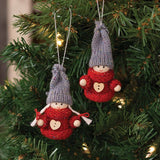 Two gnome ornaments with wooden faces, red sweaters, gray hats, and heart-shaped buttons hanging on a Christmas tree.
