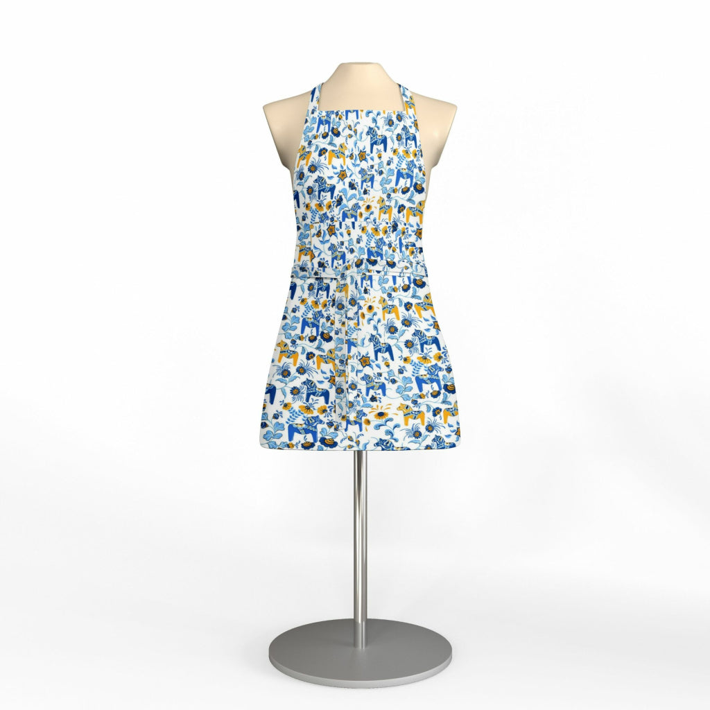 A mannequin showcases the Leksand Mini Blue & Yellow Dala Horse apron, featuring a white base with a blue and yellow abstract pattern inspired by Swedish tradition, on a stand against a plain background.