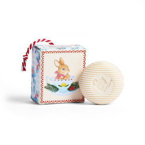 Round white bar soap with a teapot imprint next to a box featuring a bunny in a teacup illustration, tied with red and white striped string.