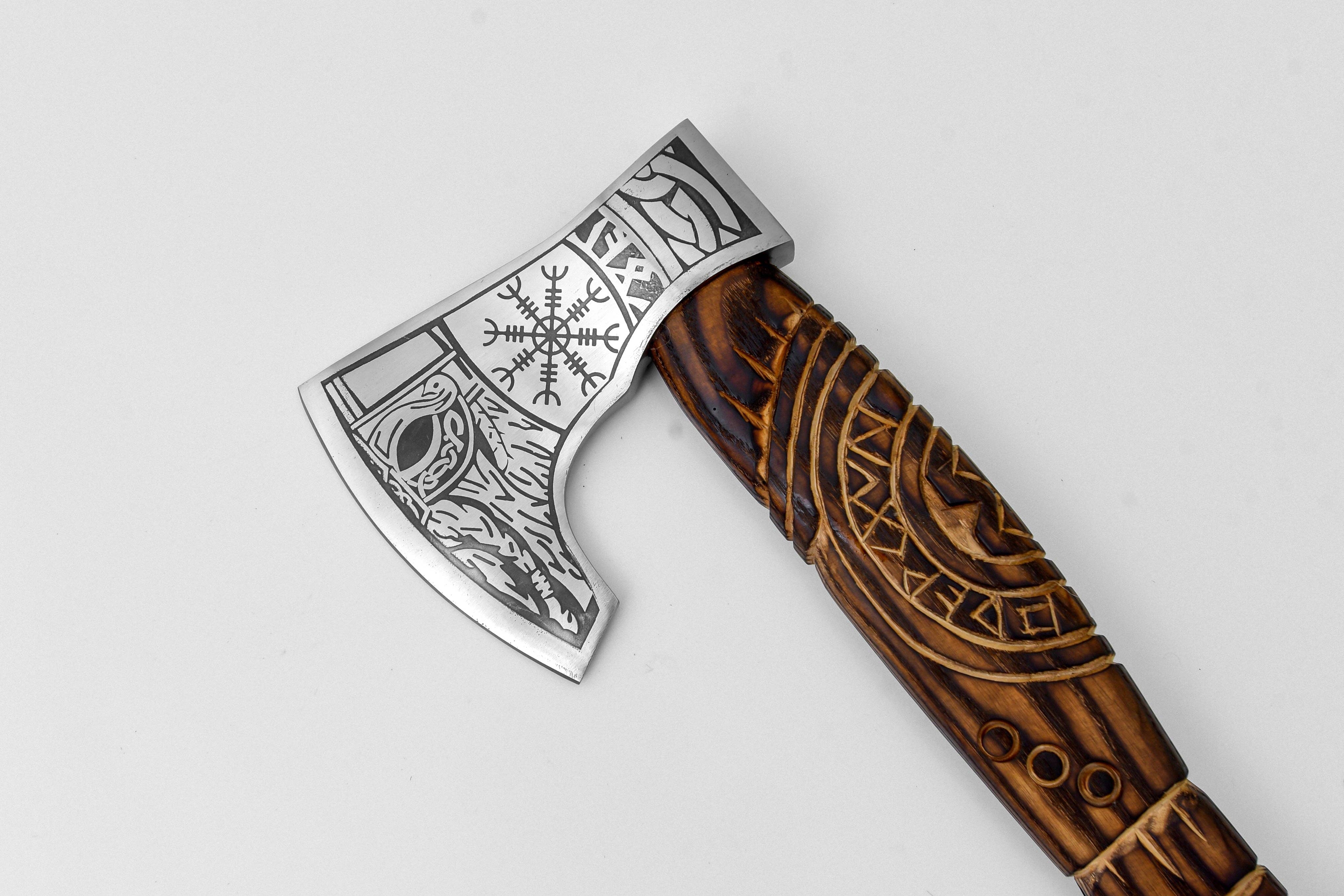 A close-up of the Axe: Aegir’s Wrath Utility Camping Tool, showcasing its carved wooden handle and engraved metal blade adorned with Norse-inspired designs and ancient runes.