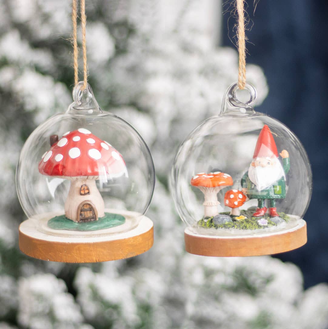 The Gnome Glass Dome ornaments elegantly display two miniature scenes: one features a red-capped mushroom house, while the other captures a gnome nestled near mushrooms in a snowy winter forest, each adorned with enchanting details that softly convey "Gnome Sweet Gnome.