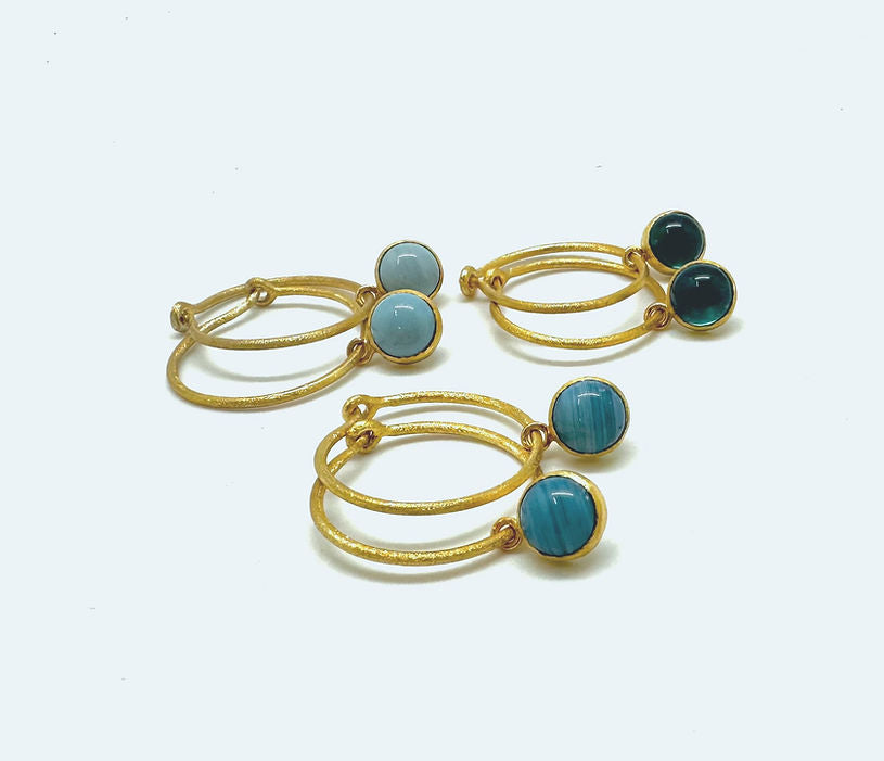 Presenting a selection of exquisite gold-plated earrings, each adorned with stunning stones: Cirkel Gold featuring the elegant Swedish Blue stone, a deep and rich dark green stone, and a vibrant turquoise stone.