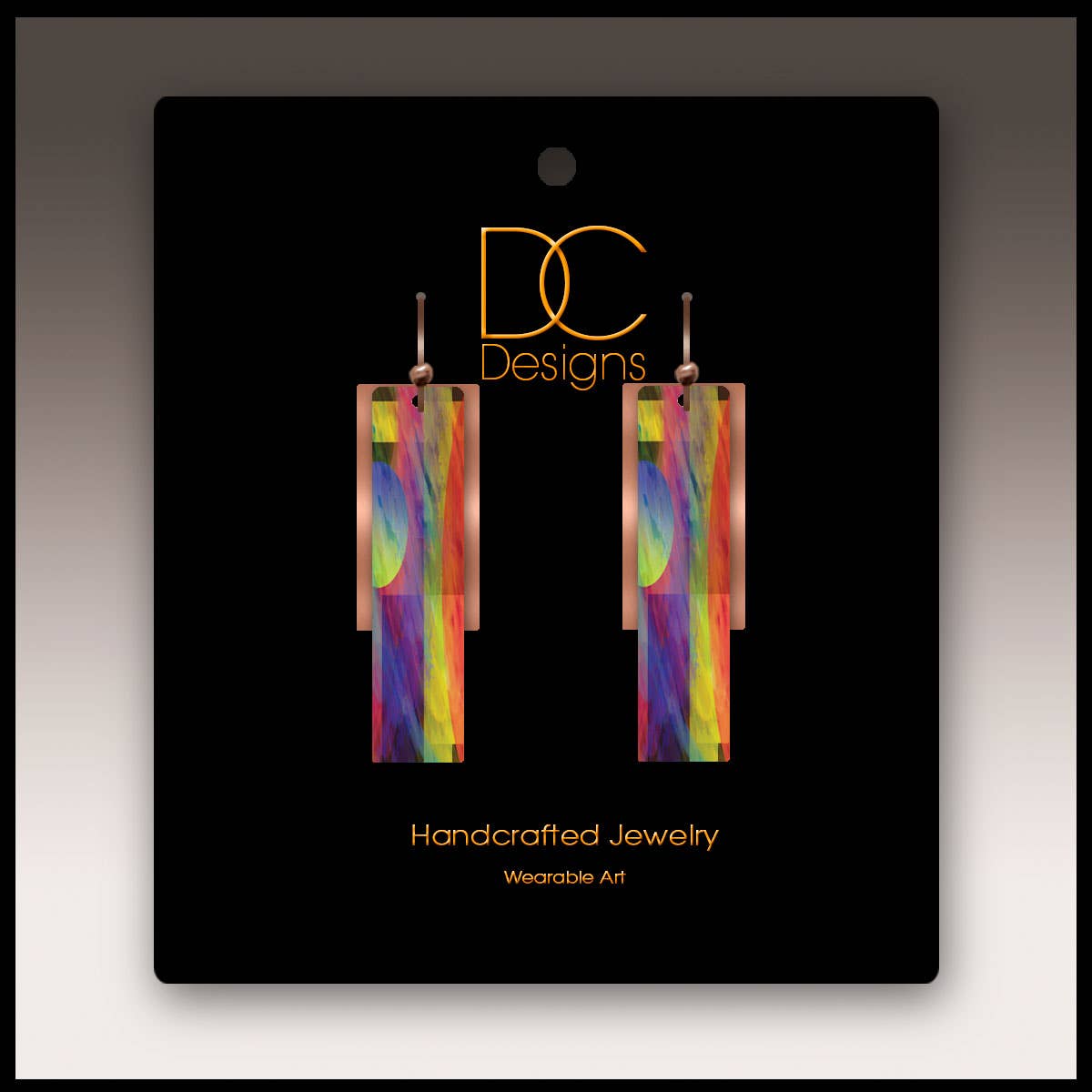A pair of multicolor copper accent multilayer earrings displayed on a black card labeled DC Designs Handcrafted Jewelry Wearable Art.