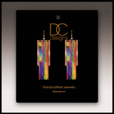 A pair of multicolor copper accent multilayer earrings displayed on a black card labeled DC Designs Handcrafted Jewelry Wearable Art.