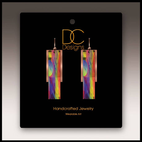 A pair of multicolor copper accent multilayer earrings displayed on a black card labeled DC Designs Handcrafted Jewelry Wearable Art.