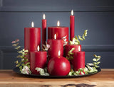 Red battery-operated candles of varying heights with 3D LED flames on a black tray with artificial eucalyptus sprigs.