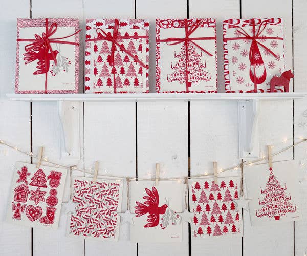 Five red and white presents on a shelf, above festive cards and ornaments, add Scandinavian charm to a white kitchen—perfectly complemented by the Scandi Christmas Tree Dish Cloth with Dala Horses & Candles for eco-friendly holiday cheer.