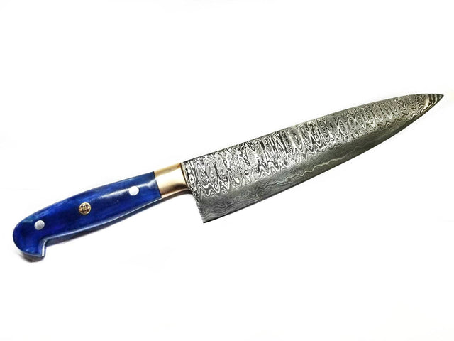 The Knife: Damascus Chef Knife features a hand-forged, patterned Damascus steel blade and a blue handle, shown on a white background.