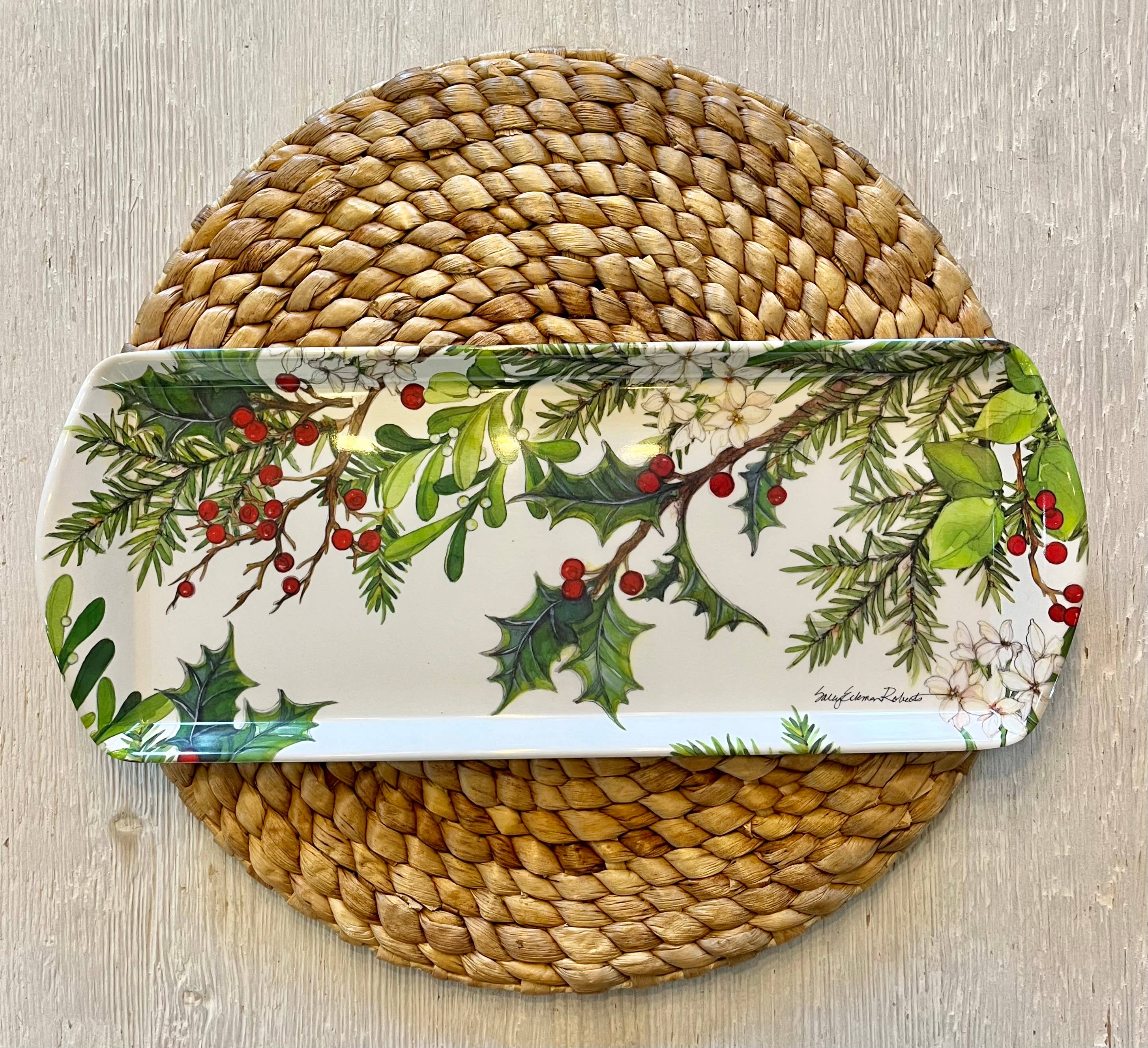The Holly & Berries Holiday Serving Appetizer, Almond Cake, Bread Loaf Tray rests on a round woven placemat atop a light wood surface.