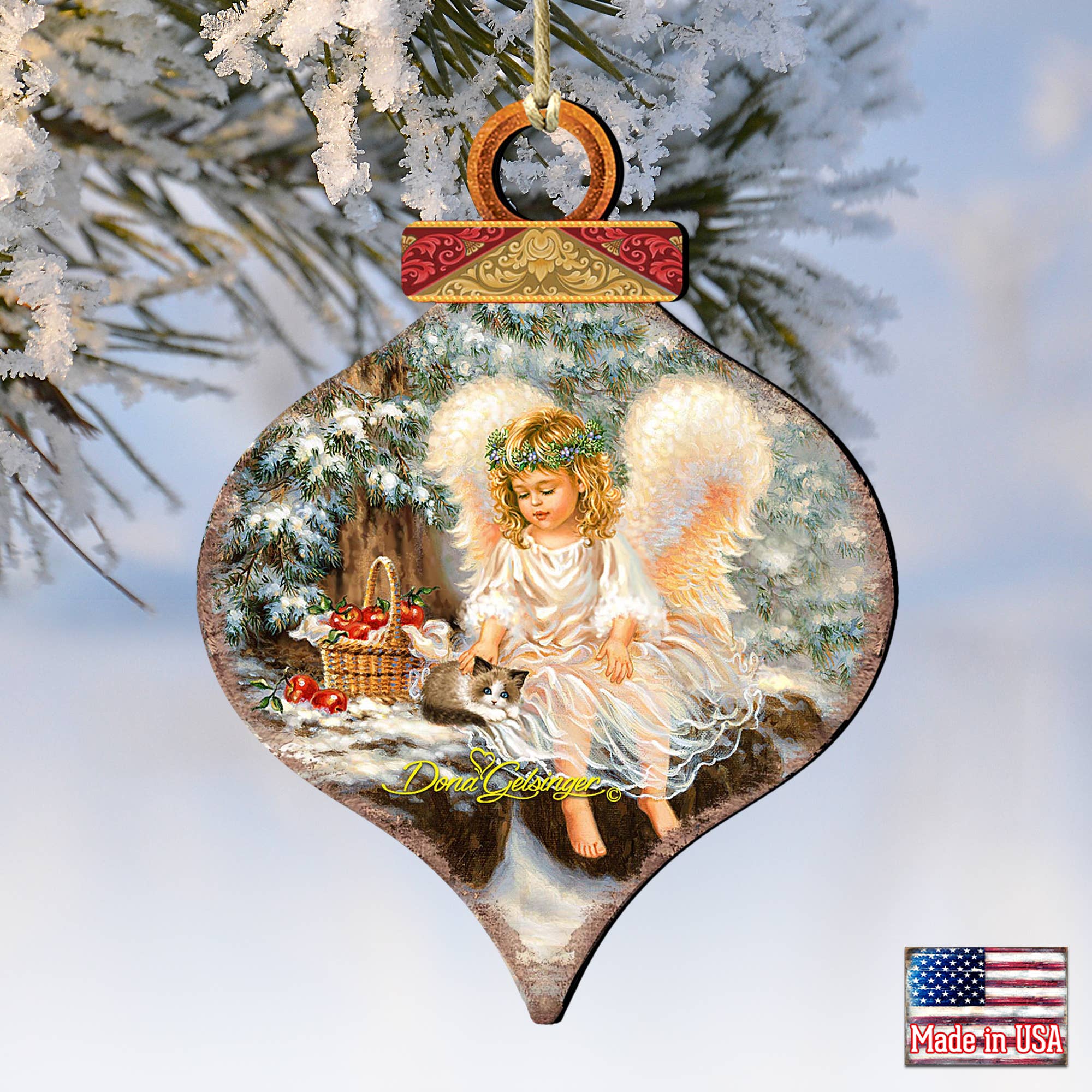 This ANGEL CARDINAL Wood Ornament from G.DeBrekht Artistic Studios, part of the Gelsinger Holiday collection, features a handcrafted design with an angel and forest scene adorned with snow and a basket of red apples, elegantly hanging from a frosted evergreen branch.