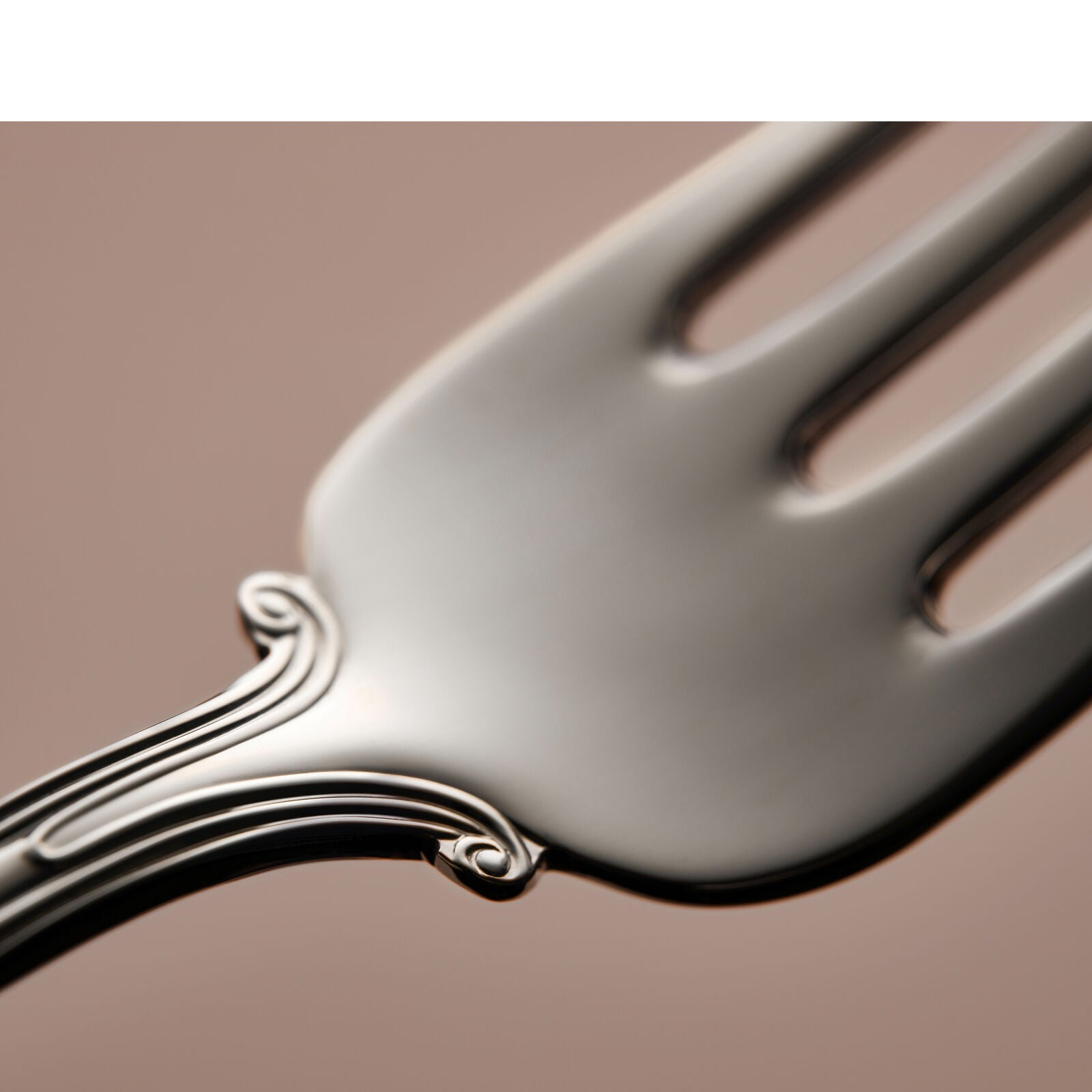 Close-up of the Gense Silver Dining Set Olga 830 forks ornate handle against a plain brown background, showcasing its detailed design.