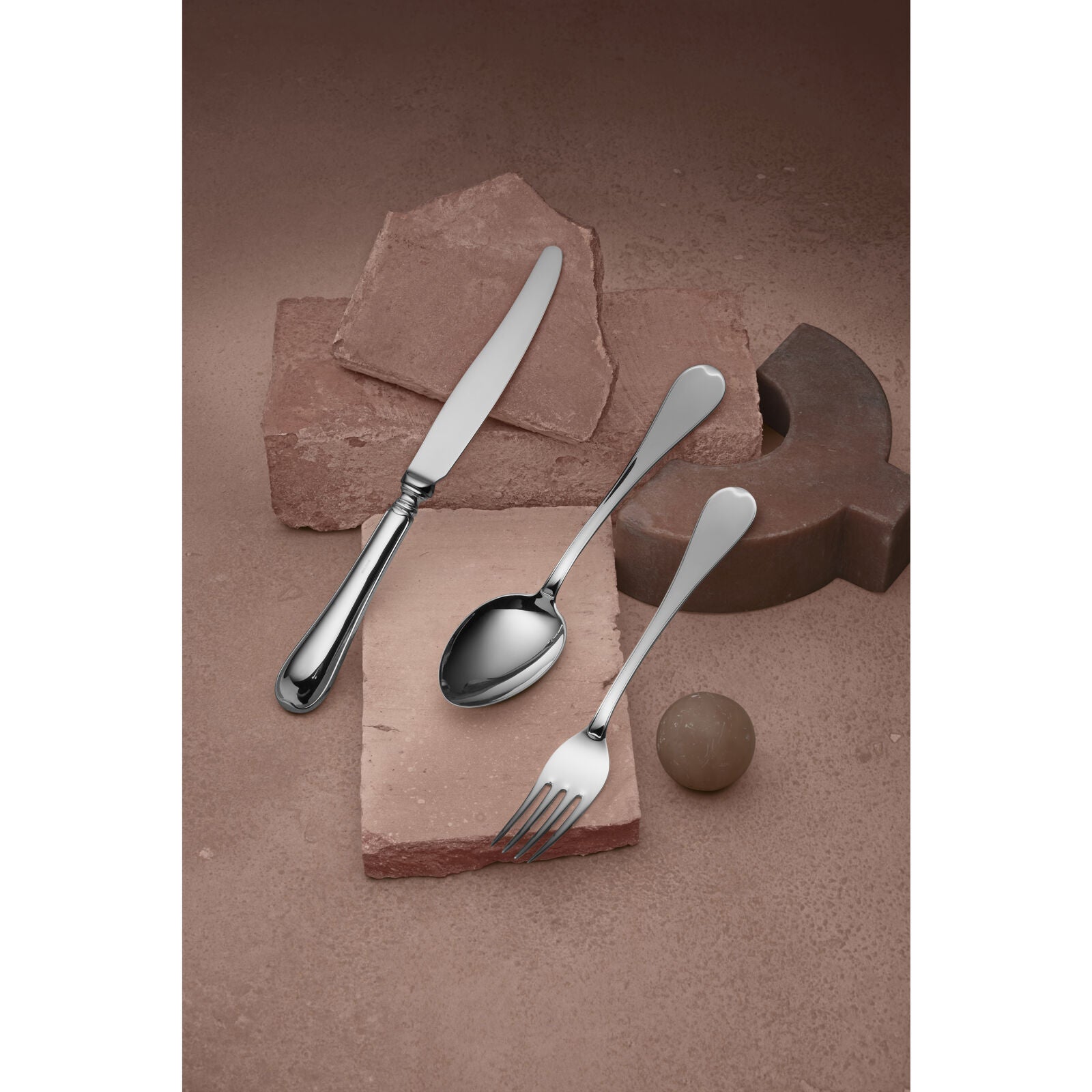 A knife, spoon, and fork from the Swedish Gense - Silver Dining Set Svensk 830 are elegantly placed on rustic stone tiles, with a small sphere and curved object in the background.