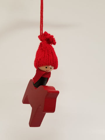 The "Ornament: Boy on Red Swedish Dala Horse" showcases a wooden figure wearing a red knit hat and scarf, suspended by a red string, embodying the charm of traditional Swedish crafts. Paired with this is the elegant red Dala Horse ornament, both exquisite pieces crafted in Sweden.