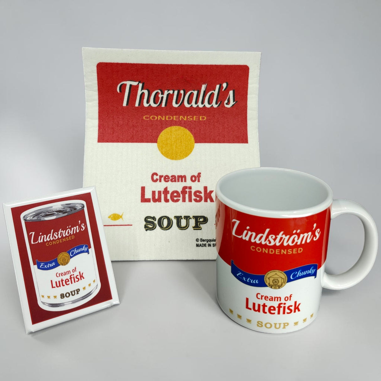 The Bundle: Cream of Lutefisk Bundle includes a card, dish towel, and vintage soup can mug with a humorous "Thorvalds Condensed Cream of Lutefisk Soup" label—unique Swedish-American souvenirs or quirky Lutefisk gifts in red, yellow, and white.