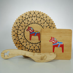 The Bundle: Dala Horse Kitchen Accessories includes three alder wood Scandinavian decor items—a heart-cutout trivet, a square cutting board, and a spatula with a Dala Horse cutout—perfect for charming kitchen style.