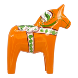Orange Swedish Dala horse made of wood, decorated with green and white painted patterns, standing upright on a white background.