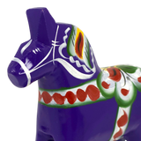Purple Swedish Dala horse made of wood with hand-painted green, red, white, and yellow patterns on its body, shown close up against a plain white background.