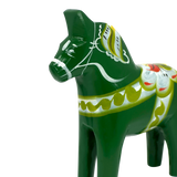 Green Swedish Dala horse figurine with white, yellow, and red painted patterns, shown on a plain white background.