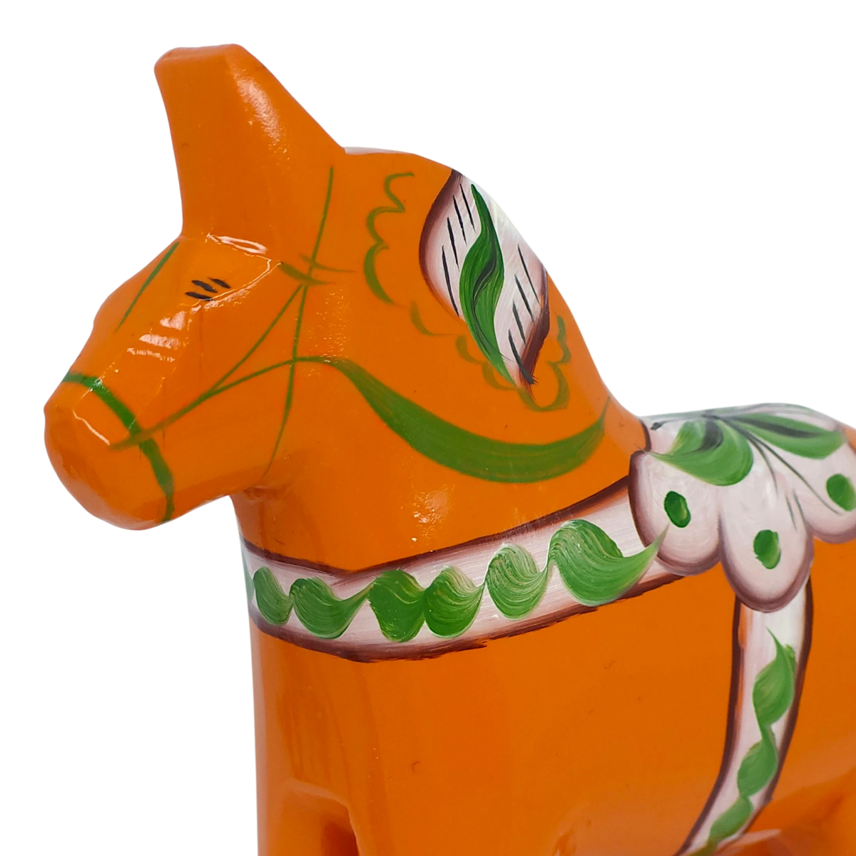Close-up of an orange Swedish Dala horse made of pine wood, decorated with green and white painted patterns, shown on a white background.