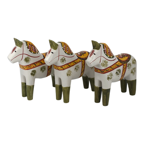 Three Dala horses with green legs, yellow and red saddles, and floral designs are arranged in a row facing left on a plain background.