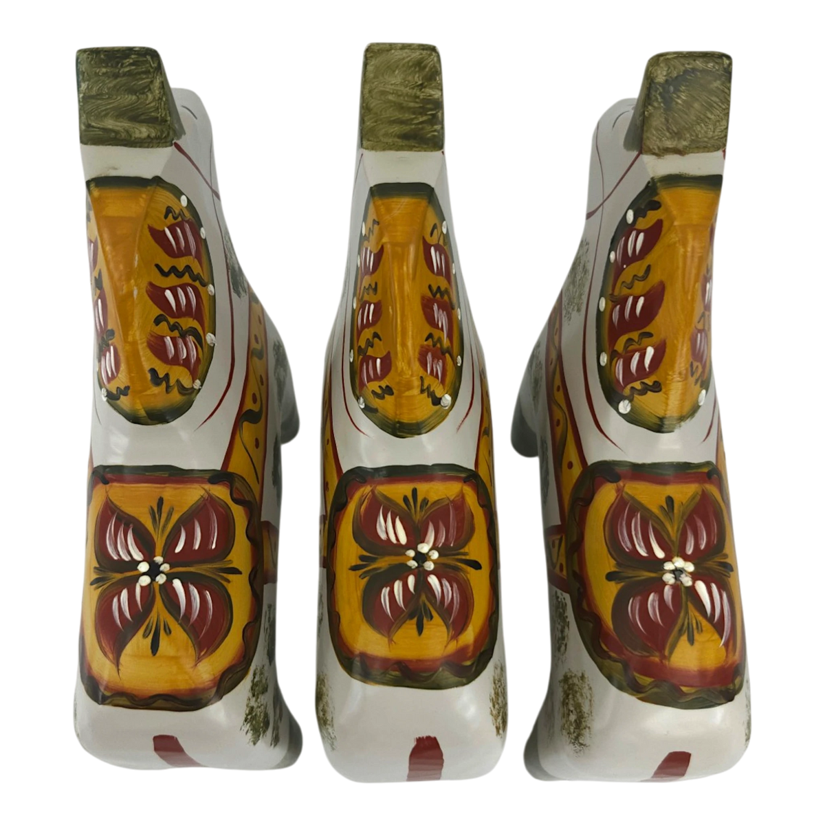 Three white hand carved wooden horses with orange, yellow, and red floral patterns on their backs, in the Swedish Dala horse style.