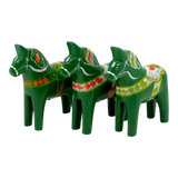 Three green Swedish Dala Horse figurines with colorful painted patterns, standing in a row and facing left on a plain white background.
