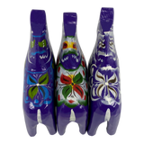 Three purple Swedish Dala horse figurines, hand-painted with colorful floral patterns on their backs, arranged side by side on a white background, viewed from above.
