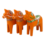 Three orange Swedish Dala horses with traditional painted patterns, arranged in a row on a white background.