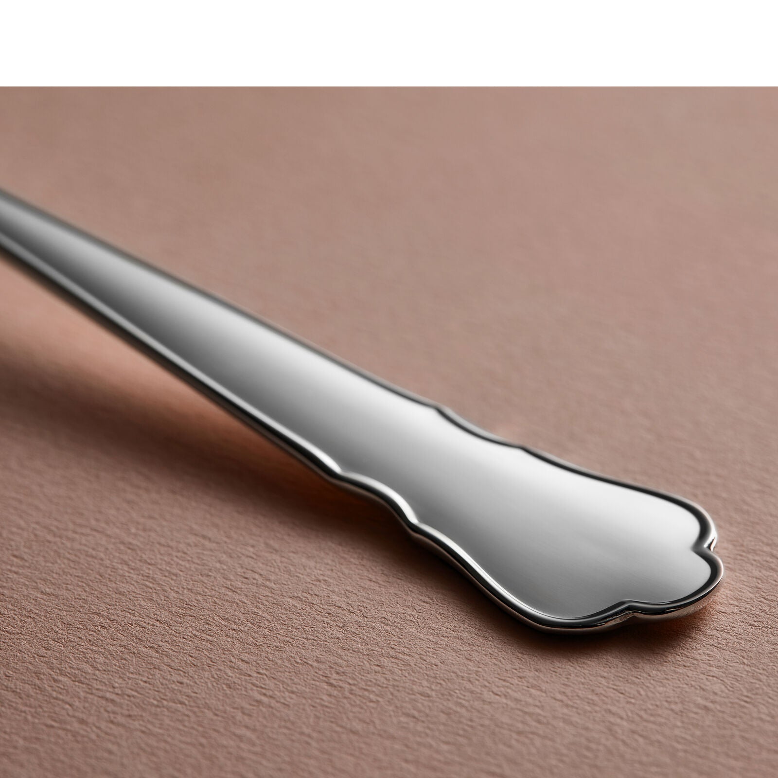 Close-up of a Gense - Silver Dining Set Chippendale 830 spoon handle, polished elegantly on a textured beige surface.