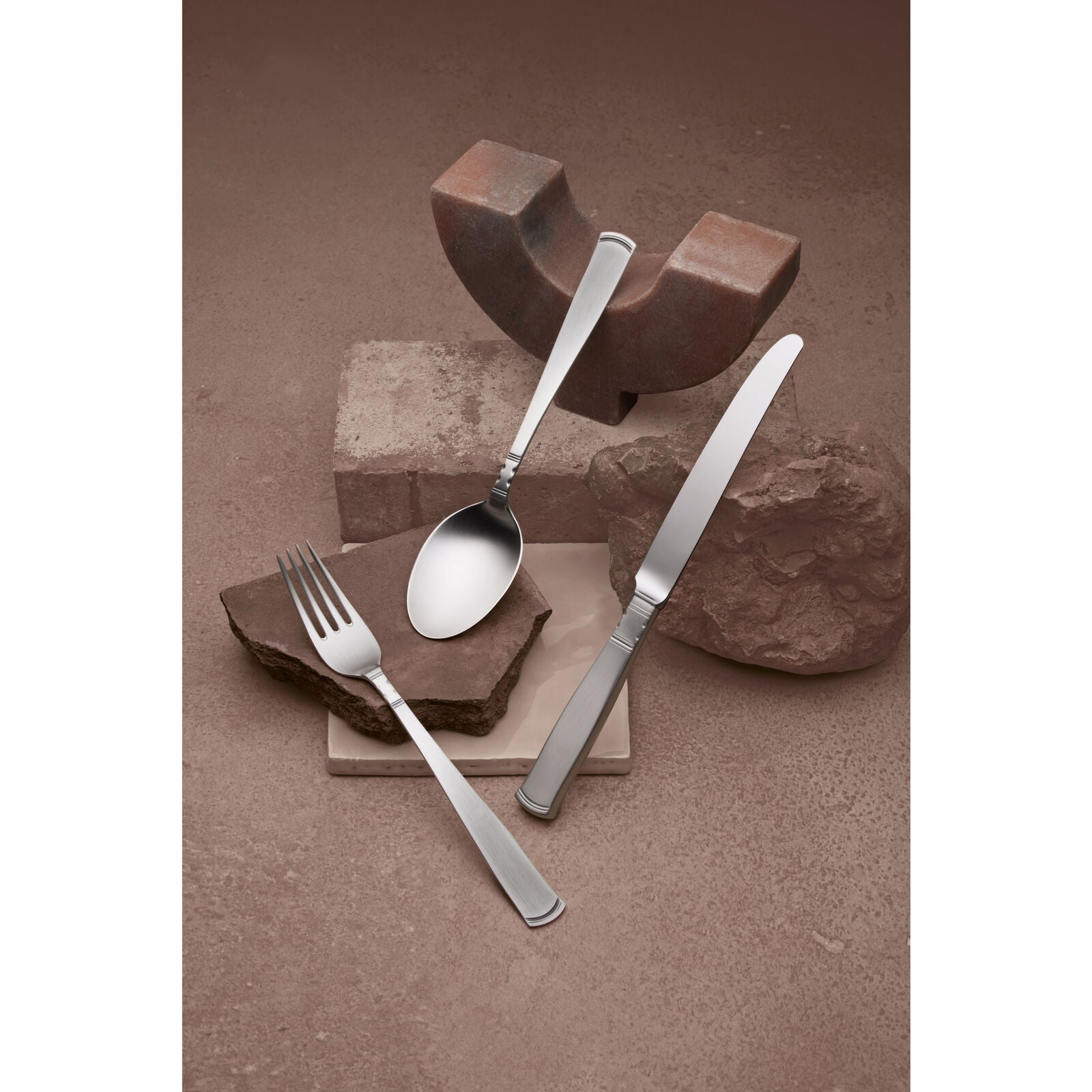 A fork, spoon, and knife from the Gense - Silver Dining Set Rosenholm 830 are artistically arranged on stone blocks against a brown background.