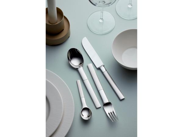 The Gense: Nobel Cutlery Set - Matte/Polished Steel, featuring an elegant Swedish design with a spoon, fork, knife, and small spoon in stainless steel, is displayed on a light blue table alongside a bowl, plate, candlestick, and wine glass.