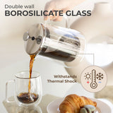 A hand pours coffee from the Kaffe French Press Coffee Maker – Double-Wall Borosilicate Glass (0.8L) into a glass mug, with a croissant on a plate nearby. Text highlights thermal shock resistance and premium materials.