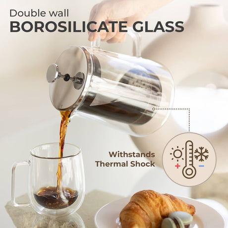 A hand pours coffee from the Kaffe French Press Coffee Maker – Double-Wall Borosilicate Glass (0.8L) into a glass mug, with a croissant on a plate nearby. Text highlights thermal shock resistance and premium materials.