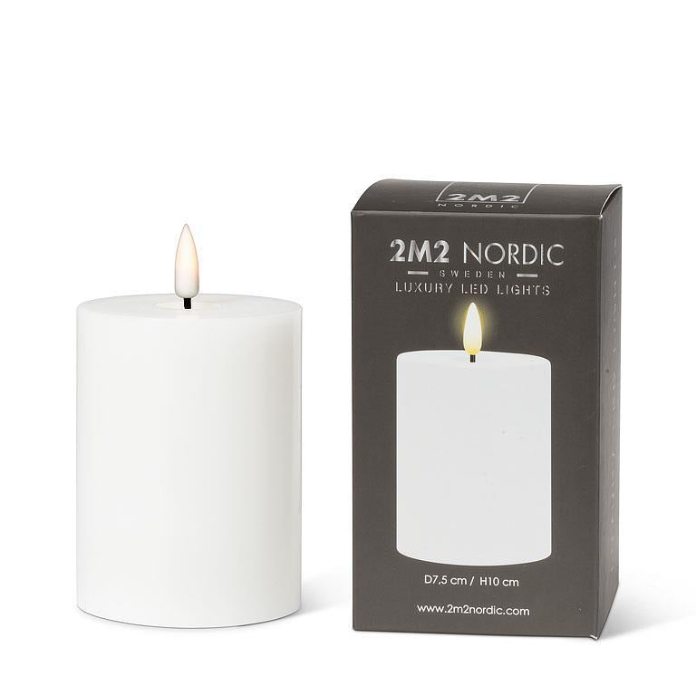 The 4" LED Pillar Candle, White rests elegantly beside its box, representing the 2M2 Nordic brand. With a realistic LED flame and dimensions of D7.5 cm / H10 cm, it provides up to 150 hours of enchanting ambiance.