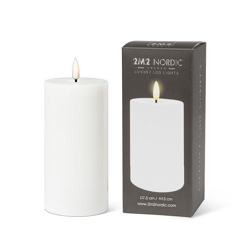 The Candle: 6" LED Pillar Candle, White, with its realistic 3D LED flame, is displayed beautifully next to its packaging box that features the product image and brand name. Offering over 150 hours of run time, it makes an ideal addition to any setting.