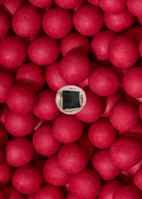 A group of red gumballs, one sliced to show a black licorice center, highlights Lakrids by Bülow - Strawberries & Cream Danish Chocolate Coated Licorice (125g), a limited edition treat inspired by Danish love.