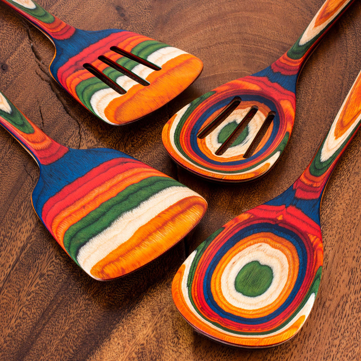 The Marrakesh Wooden Spatula – Birch, featuring vibrant layered stripes, is one of four birch kitchen utensils neatly displayed on a brown wooden surface.