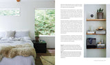 A neatly made bed sits by a window in a bright bedroom; wooden shelves hold decor against a white wall. The book Relaxed Rustic: Bring Scandinavian Tranquility & Nature into Your Home by Niki Brantmark adds to the serene, nature-inspired scene.