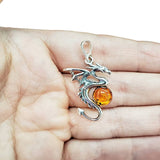 The Pendant: Cognac Amber Silver Dragon Pendant is shown resting on an open palm, featuring a striking cognac amber gemstone.