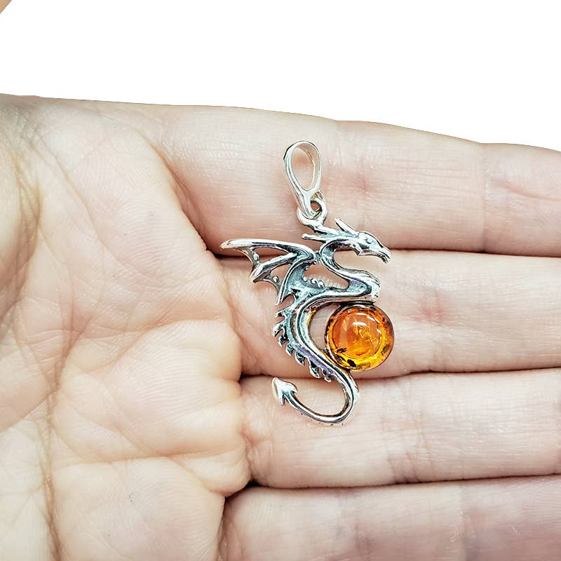 The Pendant: Cognac Amber Silver Dragon Pendant is shown resting on an open palm, featuring a striking cognac amber gemstone.